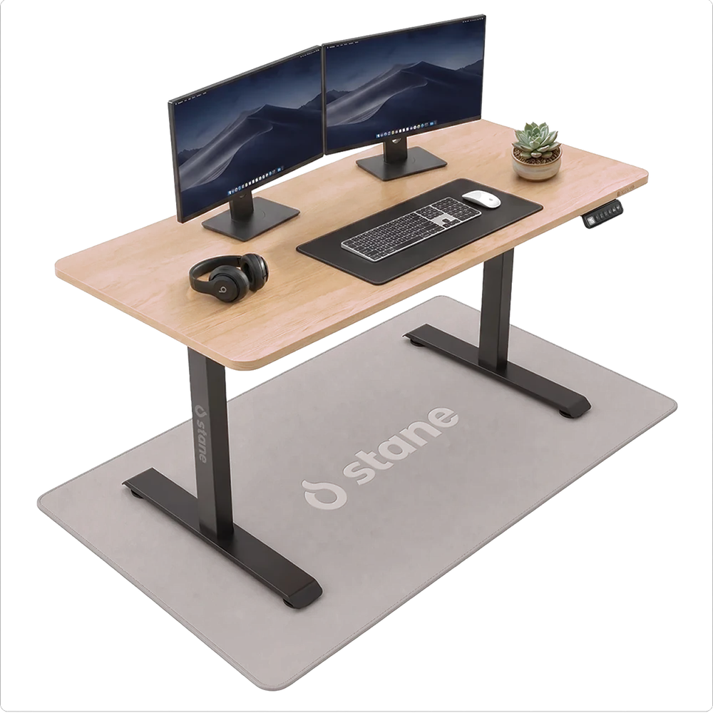 Het Stane zit-sta bureau van 120 bij 60 cm met een eiken blad en een zwart frame, vrijstaand met twee schermen, een toetsenbord en een koptelefoon erop.