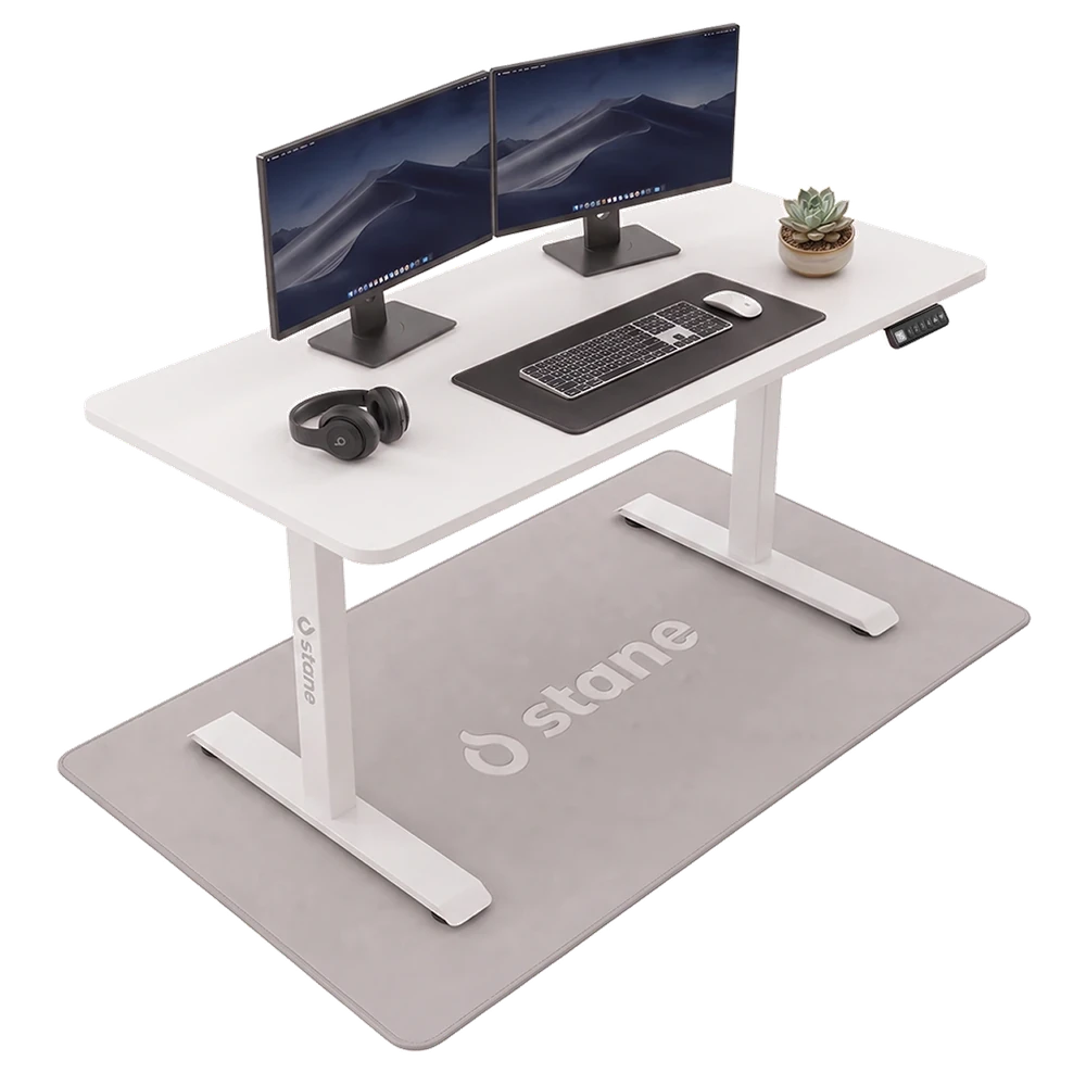 Het Stane zit-sta bureau van 120 bij 60 cm met een wit blad en een wit frame, vrijstaand met twee schermen, een toetsenbord en een koptelefoon erop.
