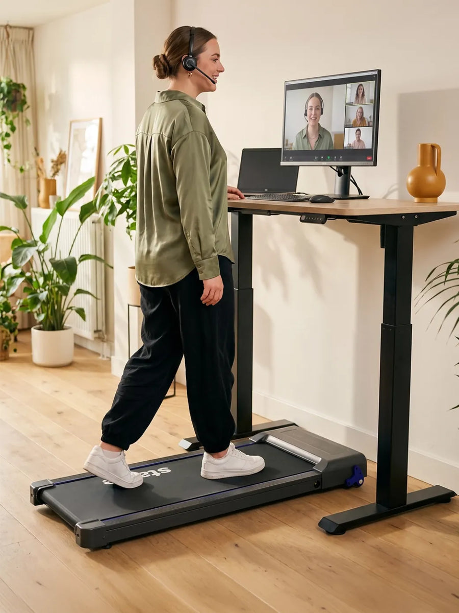 Thuiswerker met koptelefoon loopt rustig op de Stane loopband tijdens een videocall in een licht thuiskantoor