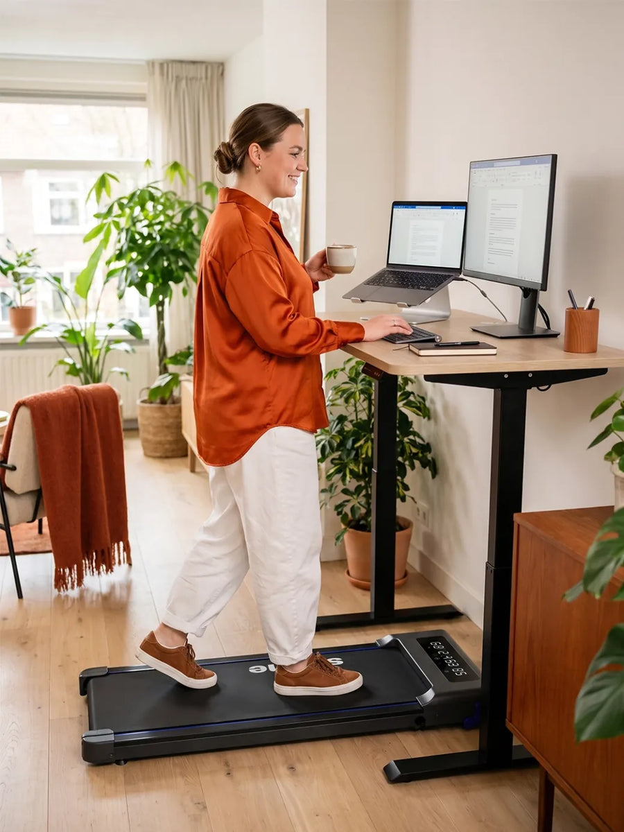 Thuiswerker typt op een laptop terwijl hij rustig op de Stane loopband wandelt aan een licht zit-sta bureau
